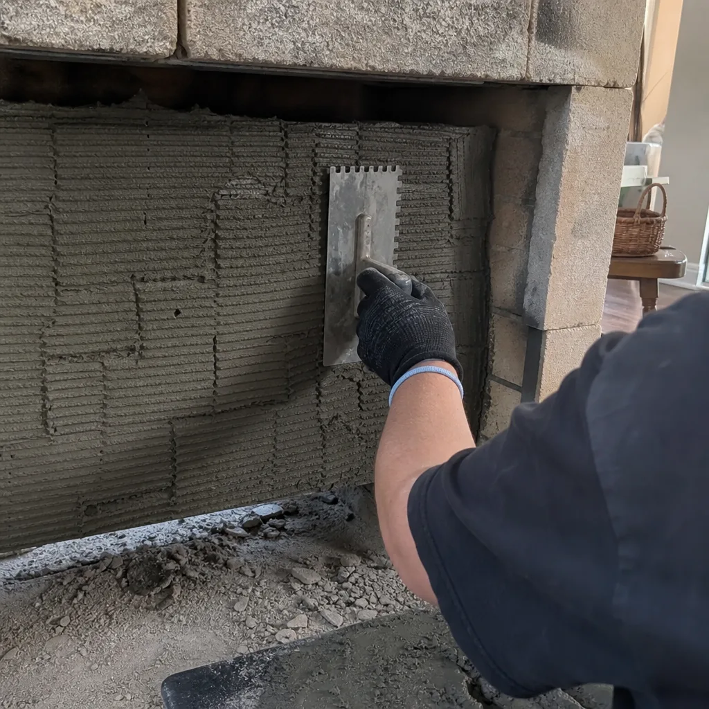 Worker applying mortar with a notched trowel to a stone fireplace
